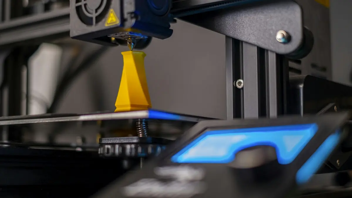 Bico de impressora 3D imprimindo uma peça amarela